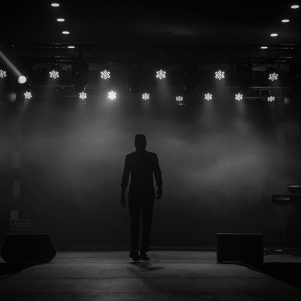 Silhouette of a man stretching against a dark background with aqua light.